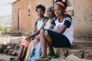 Two teenage African girls sitting on step with grandmother
