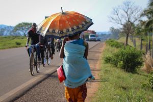 African woman walking with baby strapped to her back and with bright orange umbrella